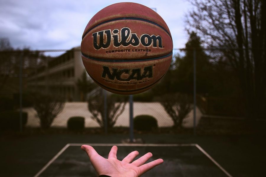 Hand tossing an NCAA basketball into the air at an outside court. Image via Dan Carlson, Unsplash.