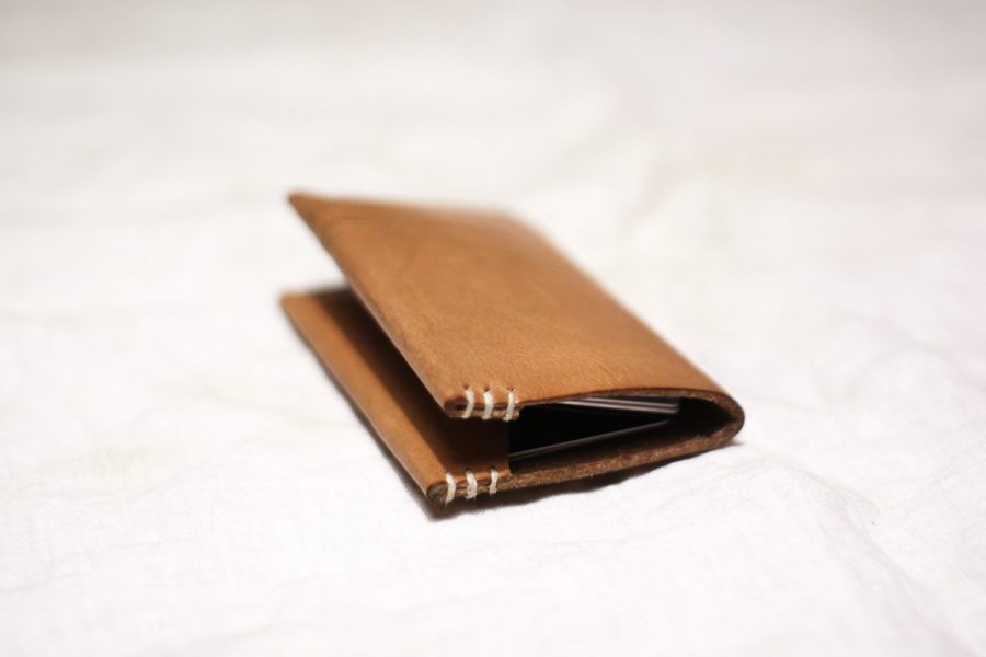 A flat wallet laying on a white counter top. the slightly open face of the wallet signifies its content are that of value.