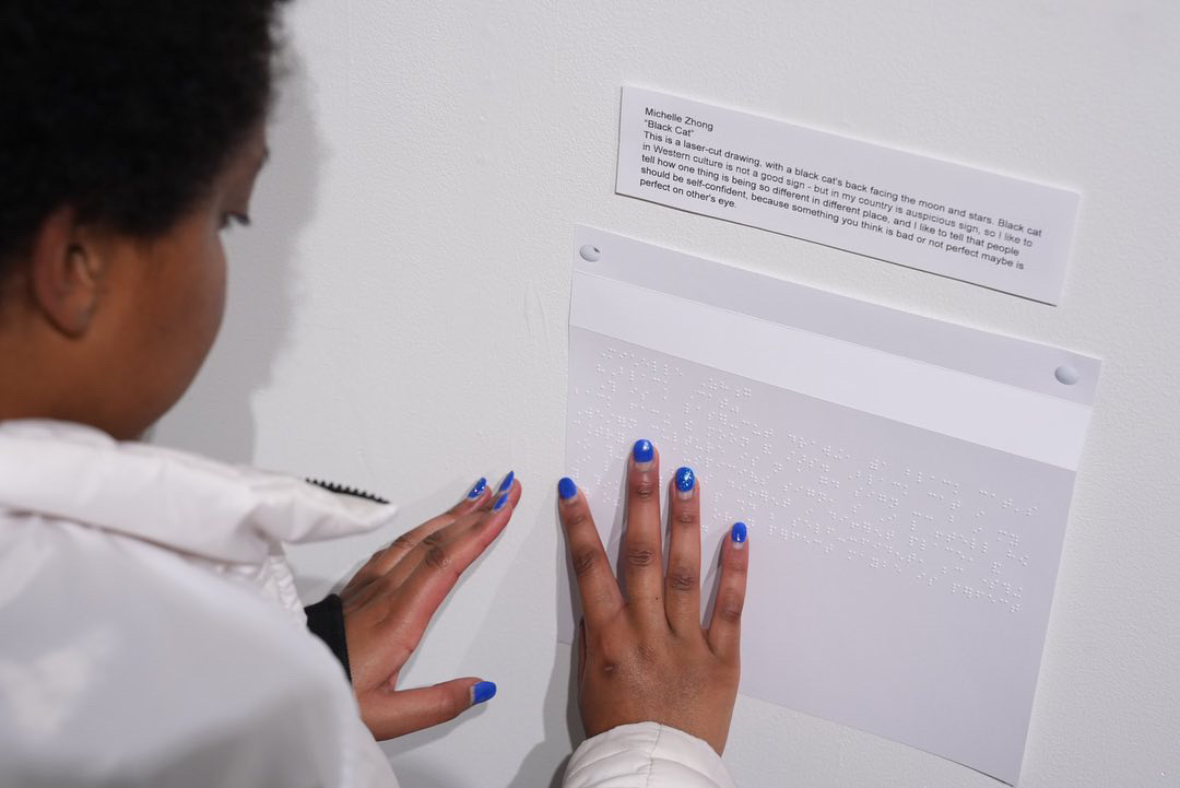 A student from the Colorado Center for the Blind reads a braille caption of an art piece.