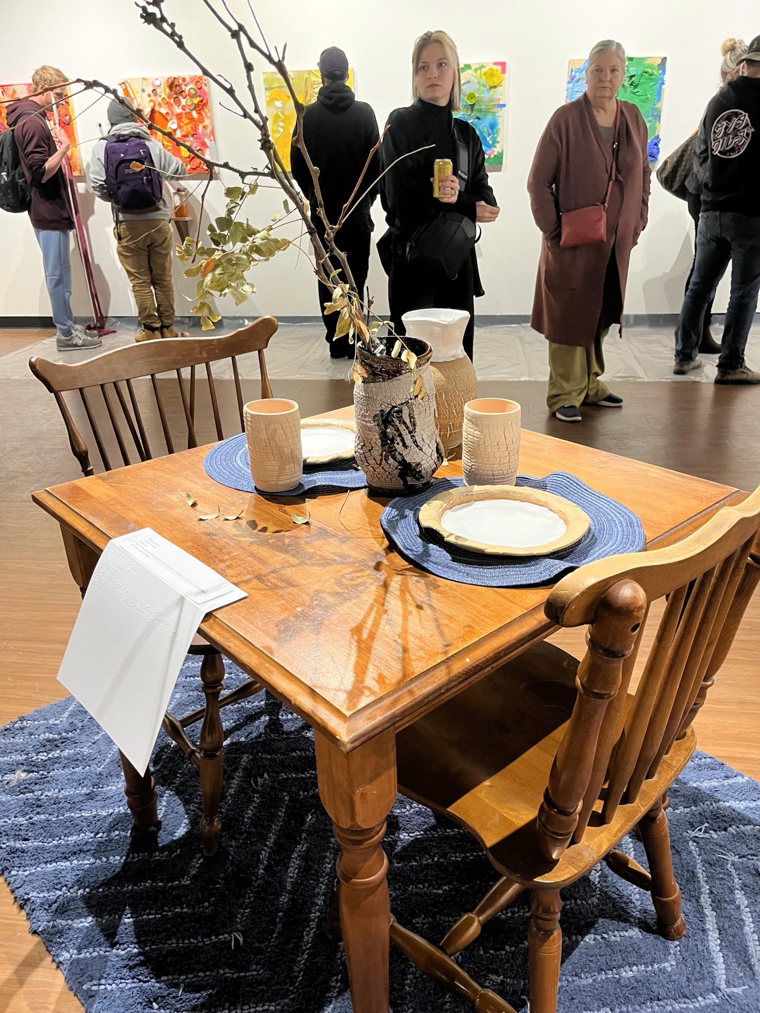Ceramics piece titled Family Dinner by Nathan Brown. Brown encorages viewers to sit at the dinner table and engage with the dinnerware as you discover the cracks and flaws that we share.